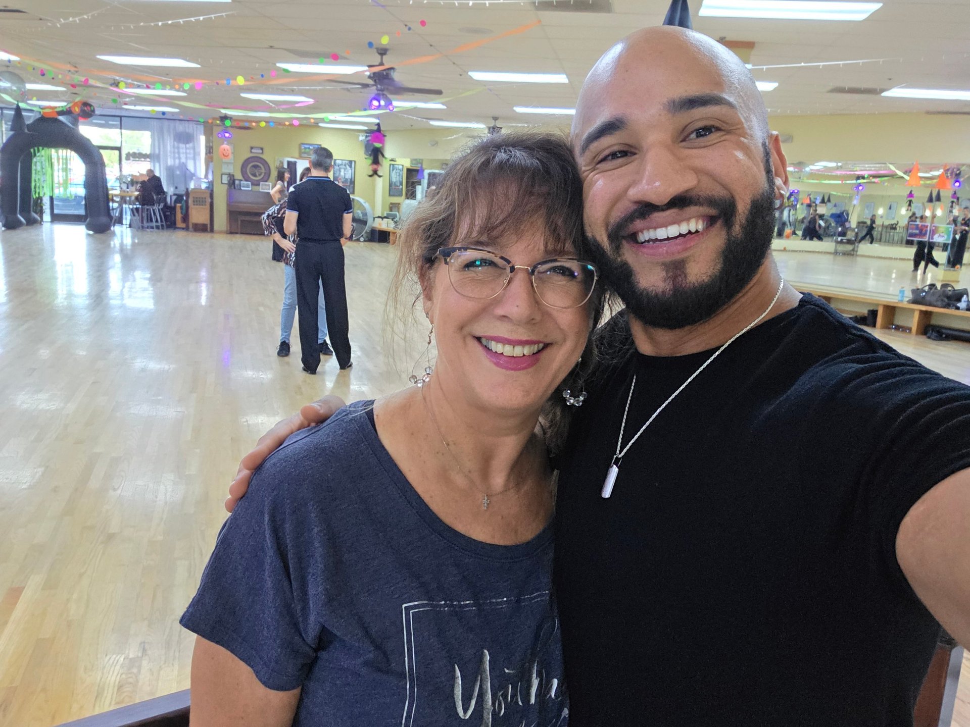 Two people smiling at camera in an indoor facility with polished flooring and other visitors in background